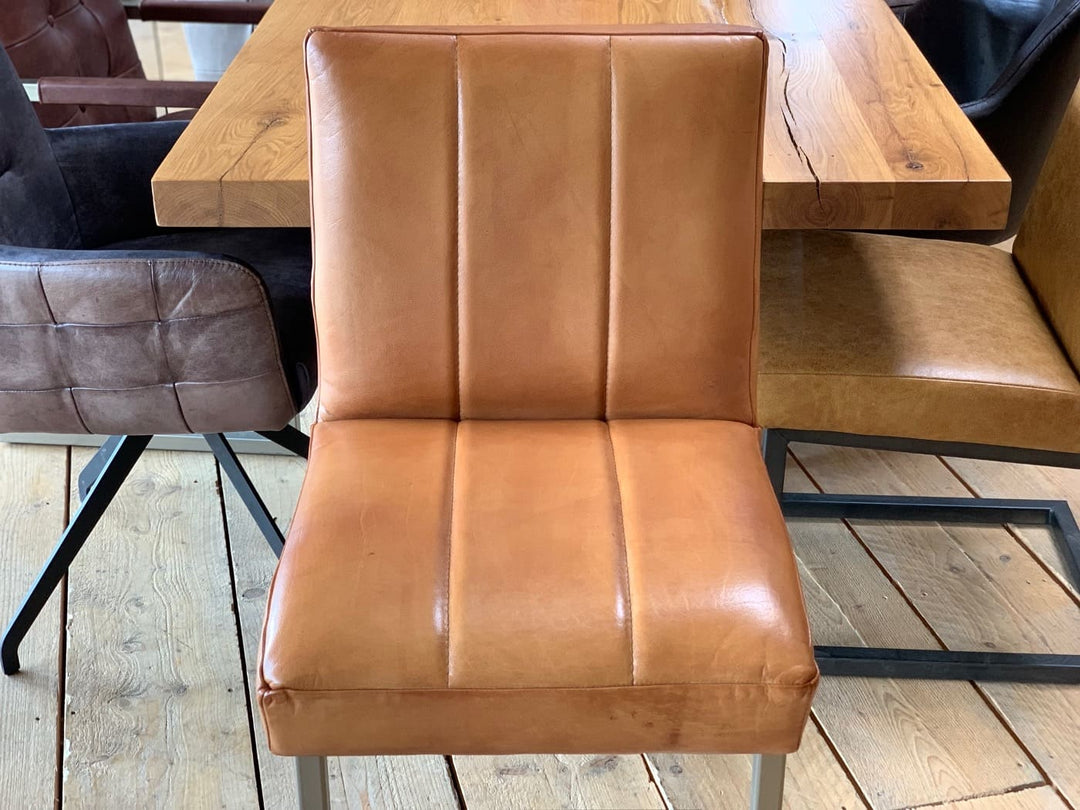 Barhocker Leder in Cognac mit gepolsterter Sitzfläche und vertikaler Steppung, Detailansicht von Sitz und Rückenlehne vor Holztisch.