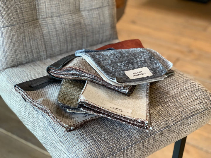Barhocker Stoffbezug Industrial Stoffauswahl: Detailaufnahme von verschiedenen Stoffmustern in Grau- und Beigetönen auf der Sitzfläche eines Barhockers, die die Auswahl an hochwertigen Stoffbezügen im Industrial-Stil zeigt.