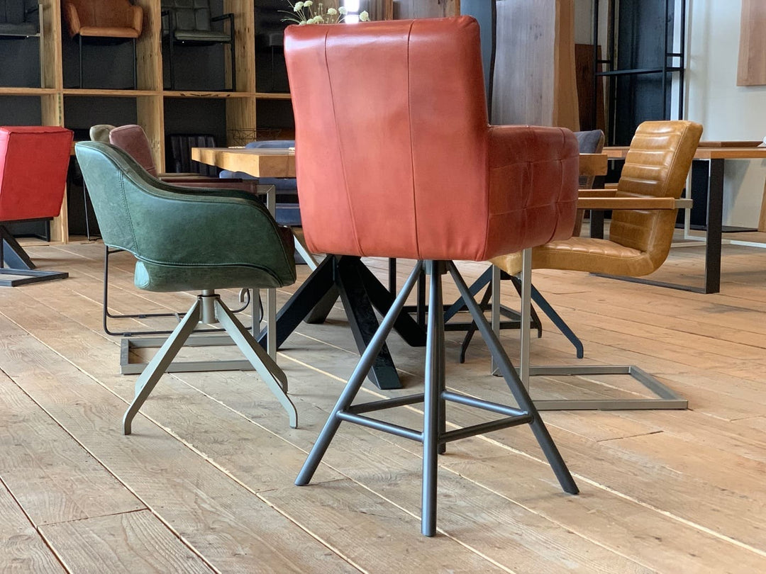 Barstuhl drehbar Leder Industrial Rückansicht: Moderner, drehbarer Barstuhl aus rotem Leder mit gepolsterter Rückenlehne und Armlehnen, kombiniert mit einem stabilen Metallgestell im Industrial-Stil, präsentiert in einem stilvollen Möbelgeschäft mit weiteren Sitzmöbeln im Hintergrund.