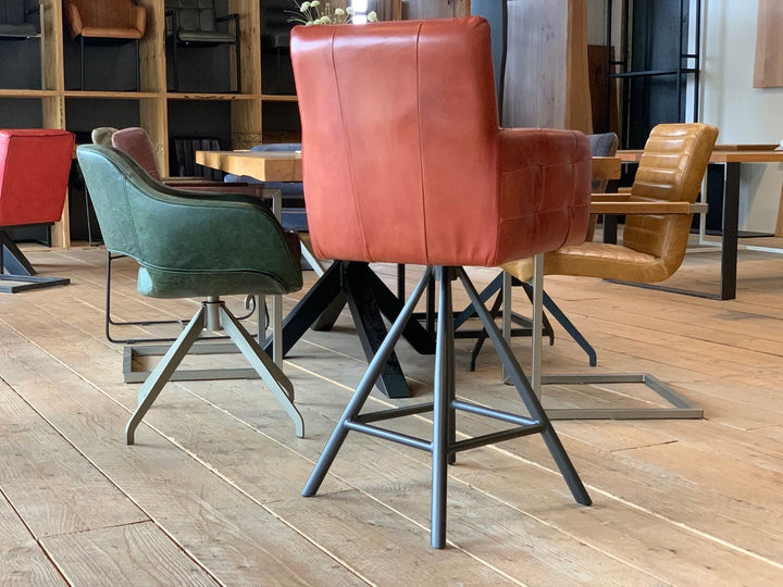 Barstuhl drehbar Leder Industrial Rückansicht: Moderner, drehbarer Barstuhl aus rotem Leder mit gepolsterter Rückenlehne und Armlehnen, kombiniert mit einem stabilen Metallgestell im Industrial-Stil, präsentiert in einem stilvollen Möbelgeschäft mit weiteren Sitzmöbeln im Hintergrund.