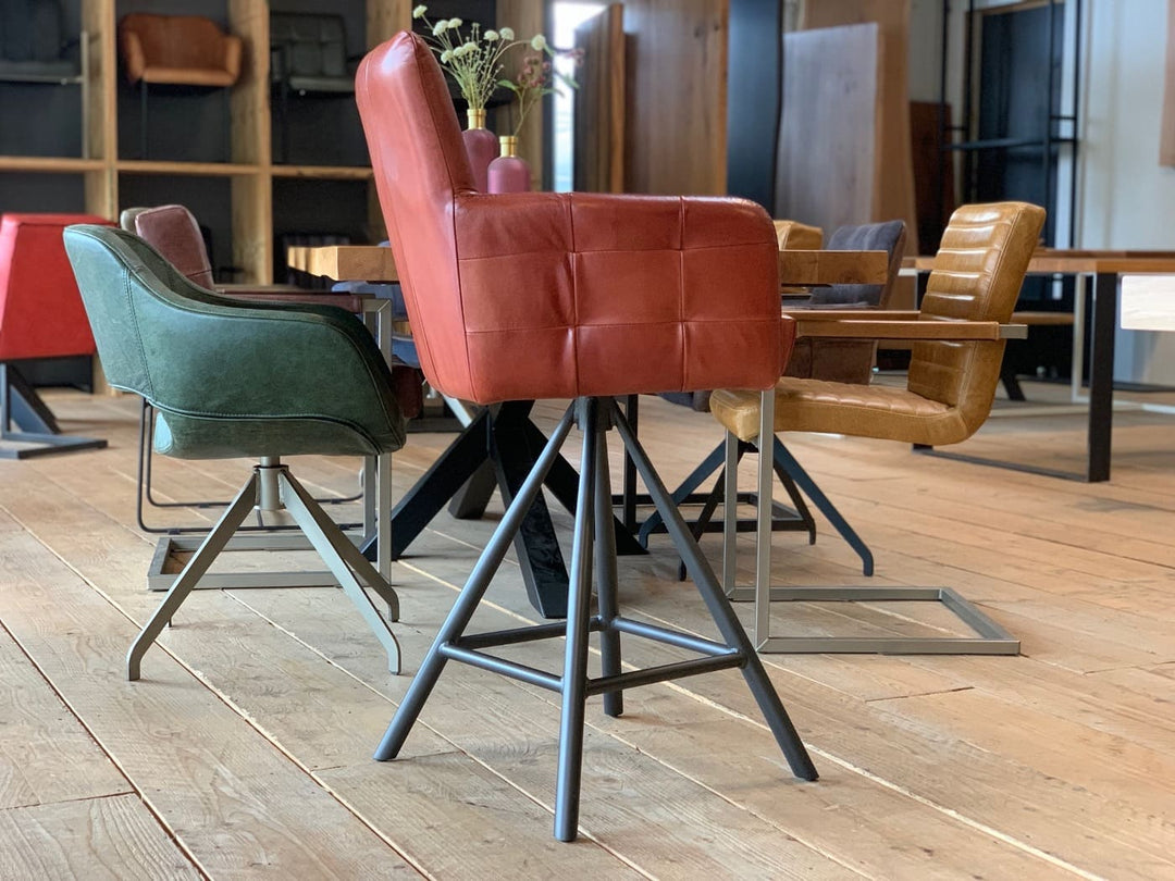 Barstuhl drehbar Leder Industrial Seitenansicht: Moderner, drehbarer Barstuhl aus rotem Leder mit gepolsterter Sitzfläche, Rückenlehne und Armlehnen, kombiniert mit einem stabilen Metallgestell im Industrial-Stil, präsentiert in einem stilvollen Möbelgeschäft mit weiteren Sitzmöbeln im Hintergrund.