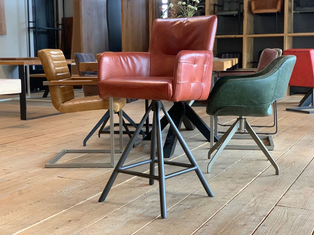 Barstuhl drehbar Leder Industrial: Moderner, drehbarer Barstuhl aus rrotem Leder mit gepolsterter Sitzfläche und Armlehnen, kombiniert mit einem stabilen Metallgestell im Industrial-Stil, präsentiert in einem stilvollen Möbelgeschäft mit weiteren Stühlen im Hintergrund.
