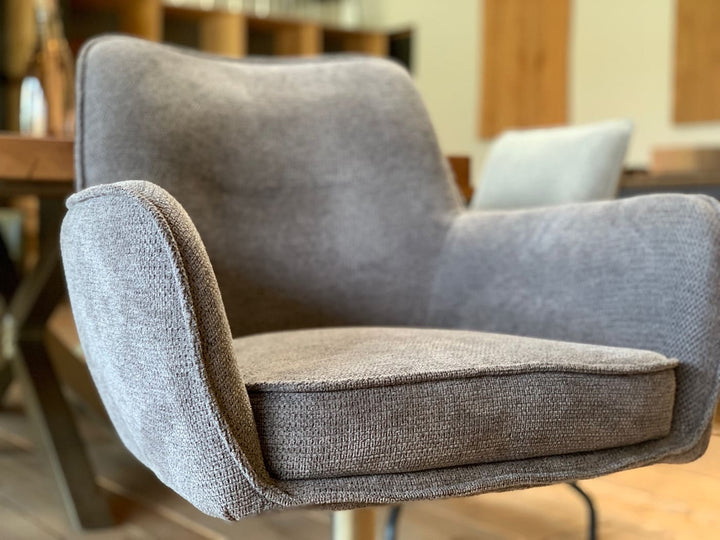 Detailaufnahme eines Designer Esszimmer-Drehstuhls mit Armlehnen, grauer Stoffbezug, weich gepolsterte Sitzfläche und hochwertige Verarbeitung im modernen Stil.