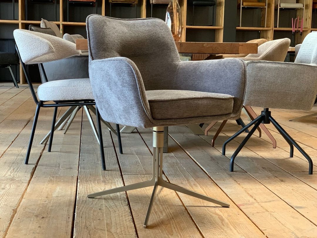 Designer Esszimmer-Drehstuhl mit Armlehnen, grauer Stoffbezug und sternförmigem Metallgestell in moderner Wohnumgebung.