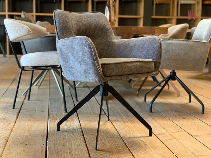 Drehbarer Essstuhl mit weichem Stoffbezug, gepolsterter Sitzfläche und schwarzem Metallgestell in modernem Esszimmer-Showroom.