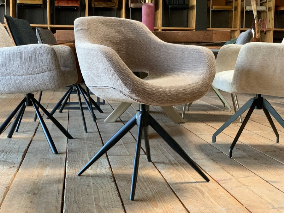 Moderner drehbarer Armlehnenstuhl mit gepolsterter Sitzschale in hellem Stoffbezug und schwarzem Metallgestell im Esszimmer-Showroom.