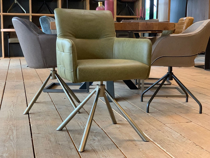 Drehbarer-Bueffelleder-Stuhl-119DS in olivgrünem Büffelleder mit gepolsterter Sitzfläche, breiten Armlehnen und stabilem Metall-Drehgestell, platziert in einem modernen Essbereich mit Holzboden und stilvollen Sitzmöbeln im Hintergrund.