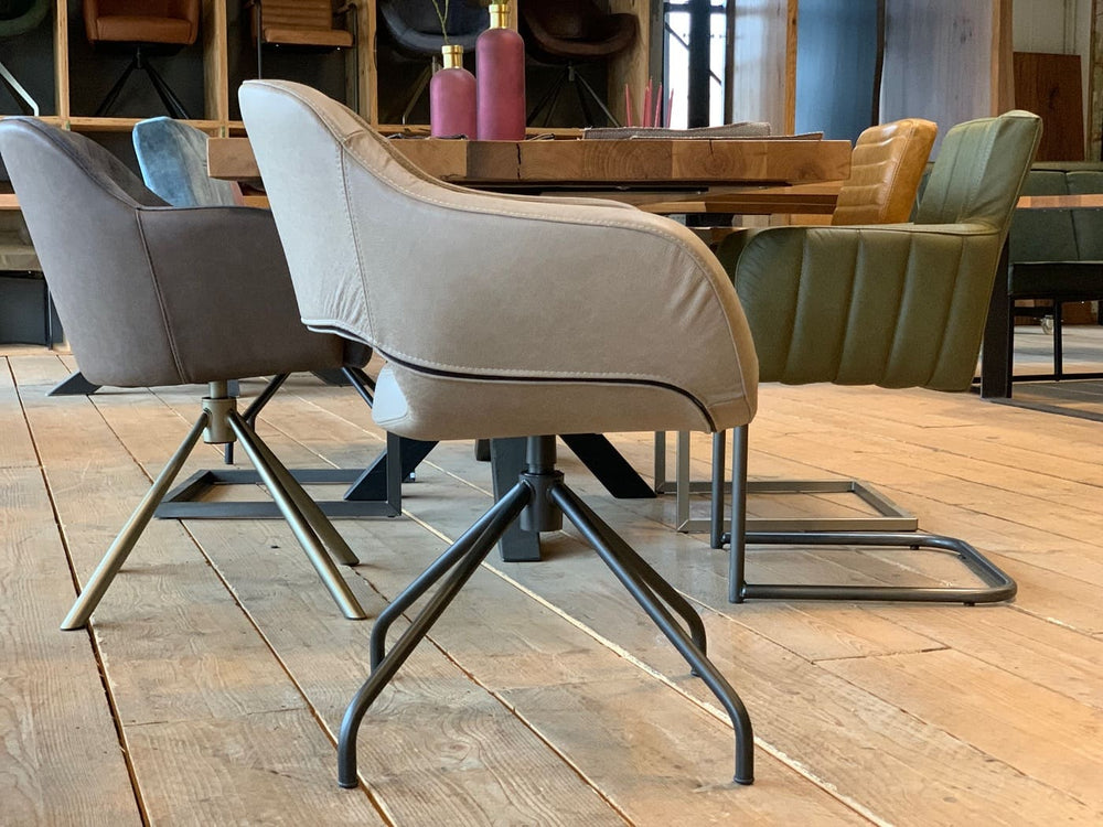 Seitliche Ansicht eines eleganten Drehbarer Lederstuhl 182D mit heller Lederpolsterung, ergonomisch geformter Rückenlehne und integrierten Armlehnen, kombiniert mit einem stabilen, drehbaren Metallgestell in moderner Sternform; platziert an einem Esstisch in einem stilvoll eingerichteten Wohnraum mit weiteren Stühlen im Hintergrund.