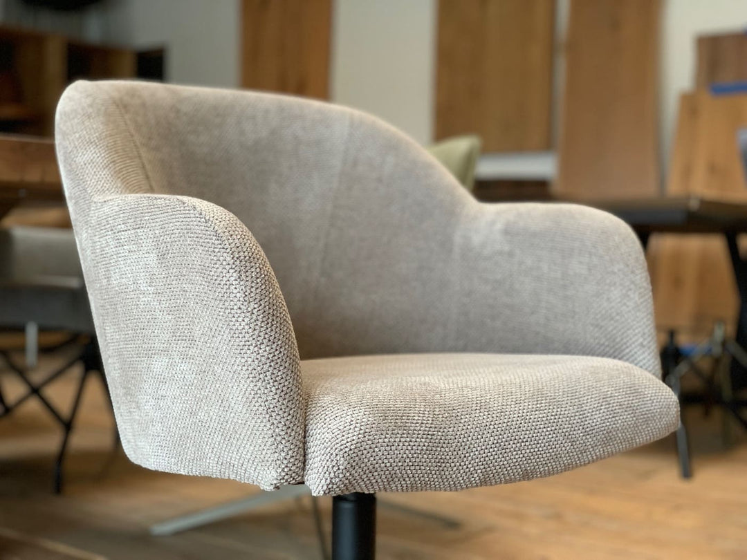 Detailaufnahme eines drehbaren Schalenstuhls mit Armlehnen in beigem Strukturstoff, weiche Polsterung und ergonomische Form