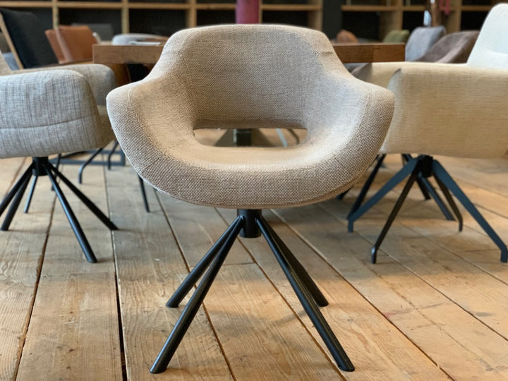Vorderansicht eines modernen Esszimmer Drehstuhls mit beigem Stoffbezug, offener Rückenform und schwarzem Metallgestell