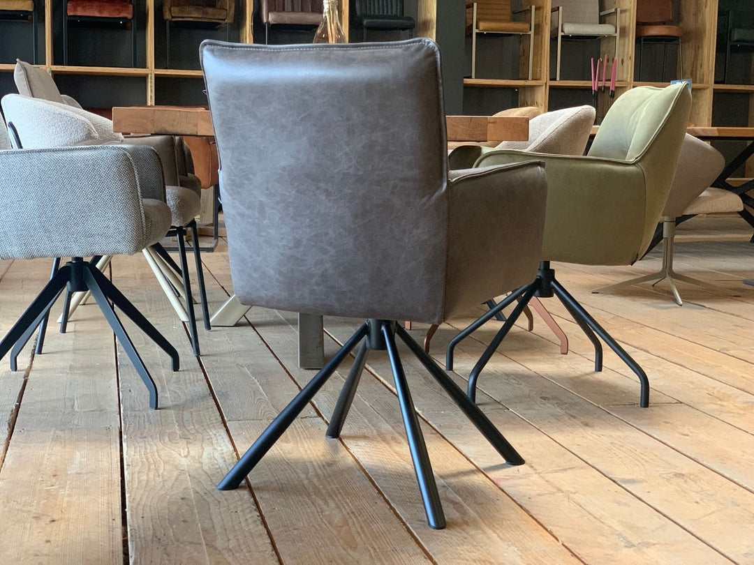 Rückansicht eines eleganten Echtleder Stuhl drehbar mit dunkler Lederpolsterung, geradliniger Rückenlehne und sauberer Nahtführung, ausgestattet mit einem stabilen, drehbaren Metallgestell in moderner Sternform; platziert an einem Esstisch in einem stilvoll eingerichteten Wohnraum mit weiteren Stühlen im Hintergrund.
