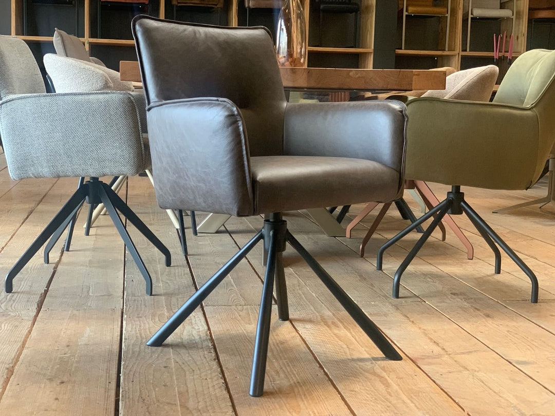 Moderner Echtleder Stuhl drehbar in dunklem Leder mit gepolsterter Sitzfläche, gerader Rückenlehne und markanten Armlehnen, kombiniert mit einem stabilen drehbaren Metallgestell in Sternform; platziert an einem Holztisch in einem stilvollen Essbereich mit weiteren Designerstühlen im Hintergrund.