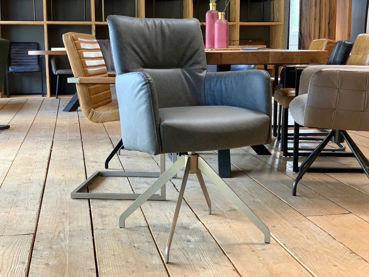 Moderner Esszimmer Drehstuhl Leder hohe Rückenlehne in Grau mit weicher Polsterung und Armlehnen, kombiniert mit einem stabilen silbernen Drehgestell, platziert an einem Holztisch im stilvollen Essbereich.