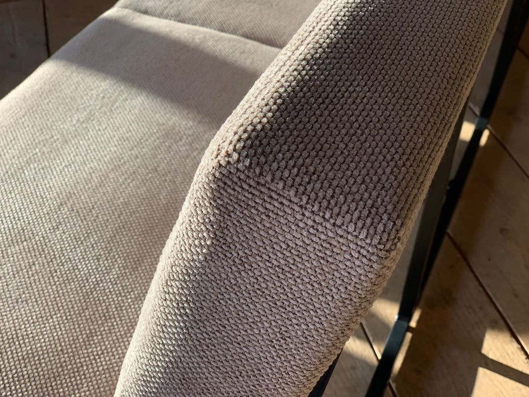 Detailaufnahme des beigen Stoffbezugs einer modernen Esszimmerbank mit strukturierter Oberfläche und weicher Polsterung im Sonnenlicht