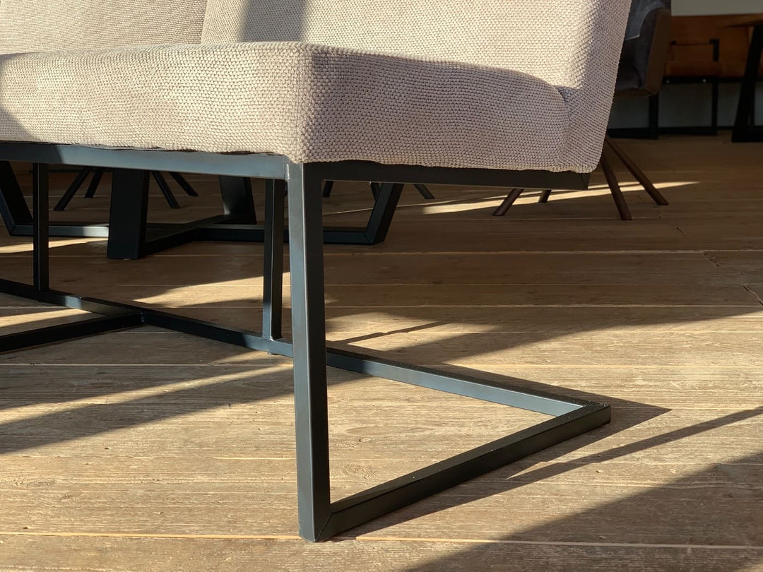 Detailaufnahme des schwarzen Metallgestells einer modernen Esszimmerbank mit beigem Stoffbezug, auf Holzboden im warmen Sonnenlicht