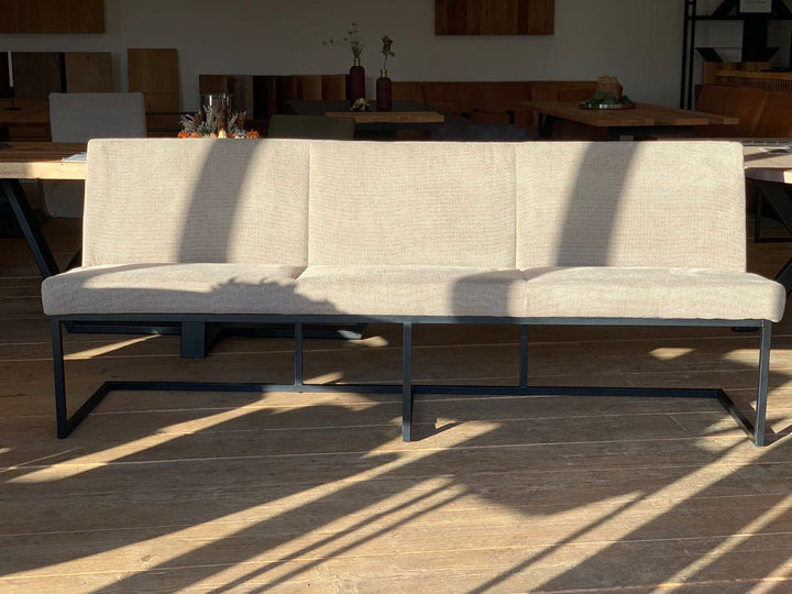 Moderne Esszimmerbank aus Stoff in Beige mit schlichter Rückenlehne und schwarzem Metallgestell, frontal im warmen Licht auf Holzboden im Essbereich inszeniert