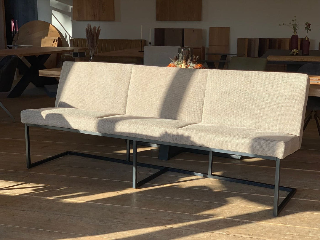 Moderne Esszimmerbank aus Stoff in Beige mit klarer Form und schwarzem Metallgestell, seitlich im warmen Sonnenlicht auf Holzboden im stilvollen Essbereich fotografiert