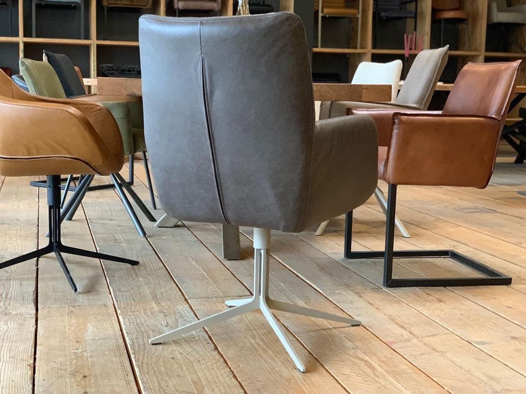 Rückansicht eines modernen Esszimmerstuhl Drehstuhl in grauer Lederoptik mit hoher, leicht geschwungener Rückenlehne und gepolsterter Sitzfläche auf einem hellen Metall-Drehgestell, platziert an einem Holztisch mit weiteren stilvollen Stühlen in einem wohnlichen Ambiente.