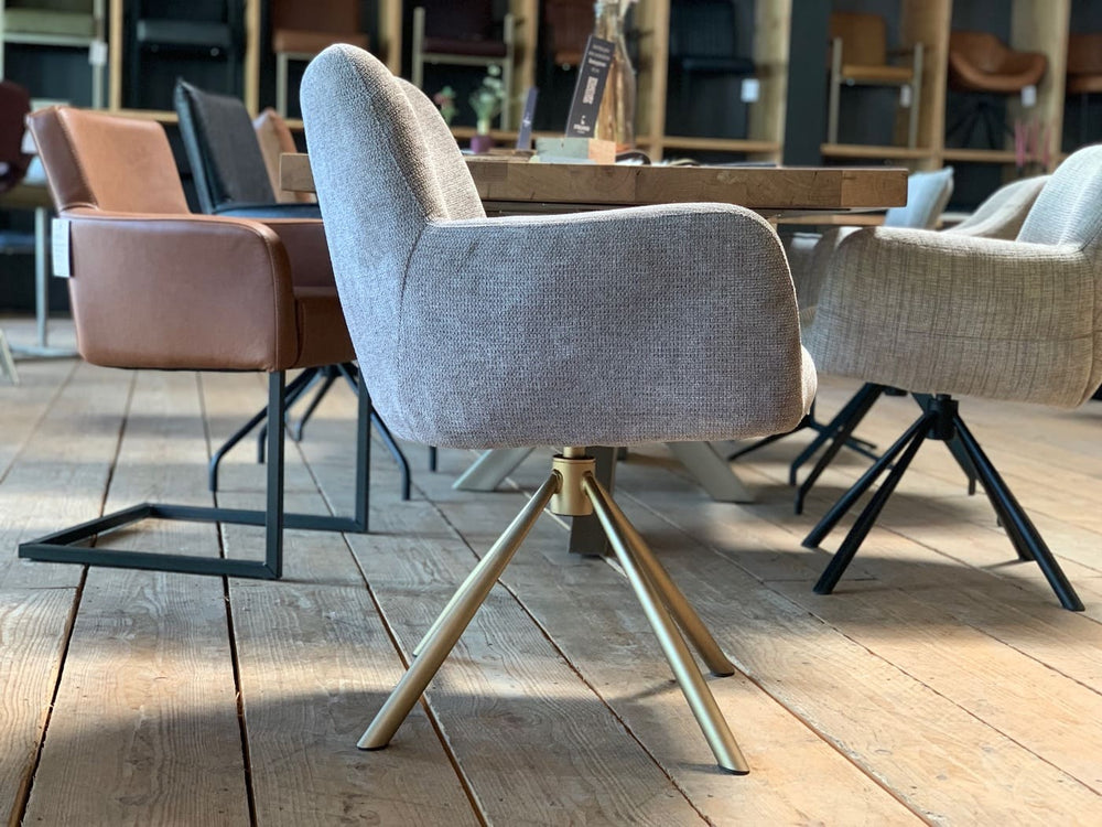 Moderner Esszimmerstuhl mit Stoffbezug und drehbarem Stahlgestell in stilvoller Seitenansicht. Die ergonomisch geformte, weich gepolsterte Sitzschale mit integrierten Armlehnen bietet hohen Komfort, während das elegante Metallgestell in warmem Finish für Stabilität sorgt und dem Stuhl eine leichte, zeitgemäße Optik verleiht – ideal für moderne Essbereiche.