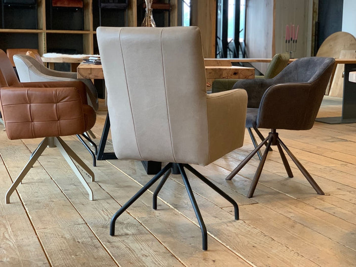 Esszimmerstuhl drehbar aus Leder in Taupe mit Armlehnen in Rückansicht, an einem Holztisch in moderner Wohnumgebung mit weiteren gepolsterten Stühlen auf hellem Holzboden.
