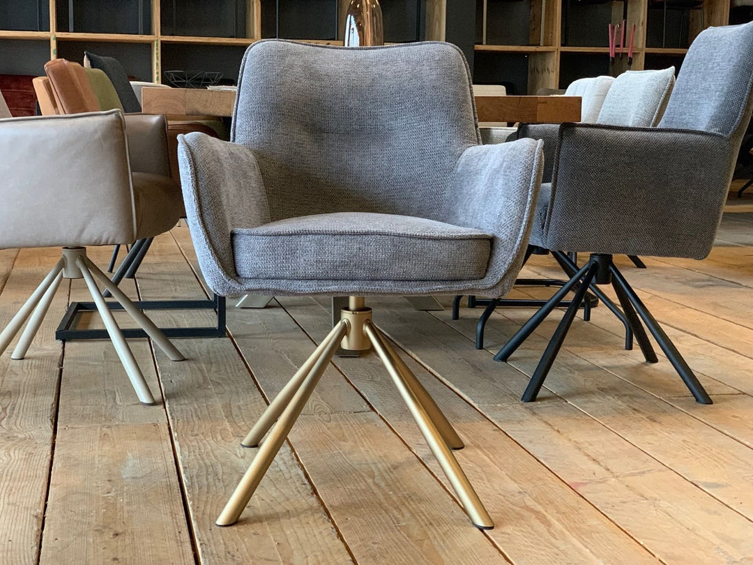 Drehbarer Esszimmerstuhl mit Armlehnen in Vorderansicht, grauer Stoffbezug und modernes Metallgestell in Goldoptik, platziert in einem stilvollen Esszimmer.