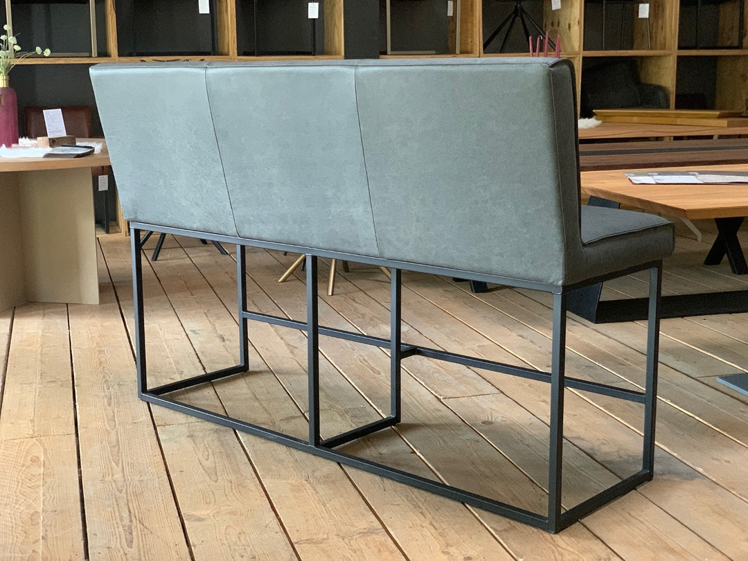 Hochbank aus Leder mit grauem Bezug und hoher Rückenlehne, Rückansicht mit stabilem schwarzem Metallgestell im Industrial-Design in moderner Wohnumgebung.