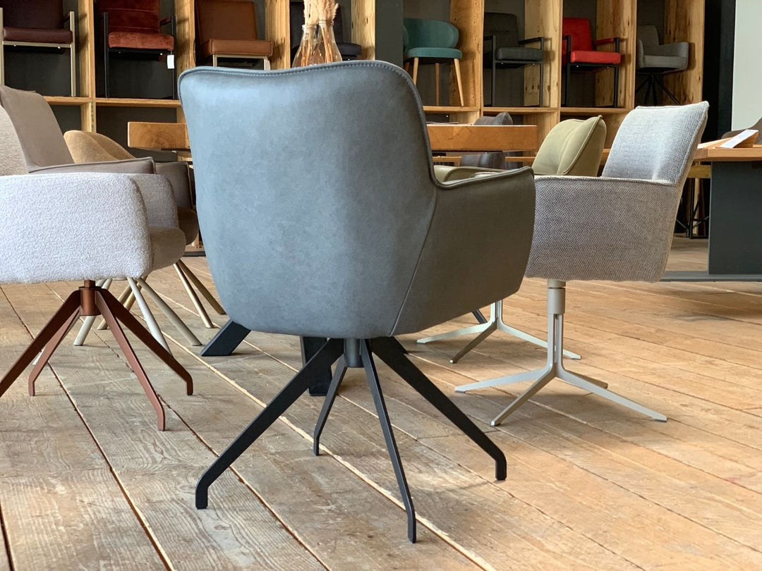 Rückansicht eines hochwertigen Drehstuhls aus Leder mit Armlehnen und markantem Metallgestell, modern inszeniert in einem stilvollen Showroom.