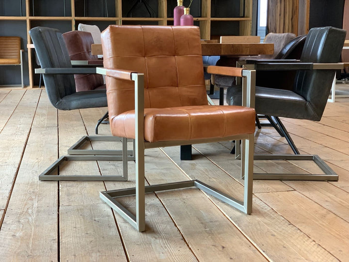 Industrial Freischwinger Leder mit gepolsterter Sitzfläche und Rückenlehne in cognacfarbenem Echtleder Vintage Cognac mit dezenter Karosteppung. Der Stuhl steht auf einem rechteckigen Kufenuntergestell in Edelstahloptik.