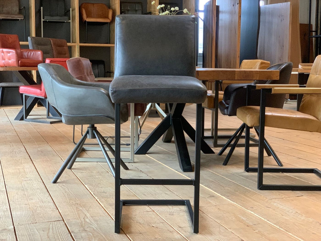 Barhocker Leder schwarz in Vorderansicht mit gepolsterter Sitzfläche und stabilem Metallgestell, im modernen Essbereich mit Holztisch und Designerstühlen.