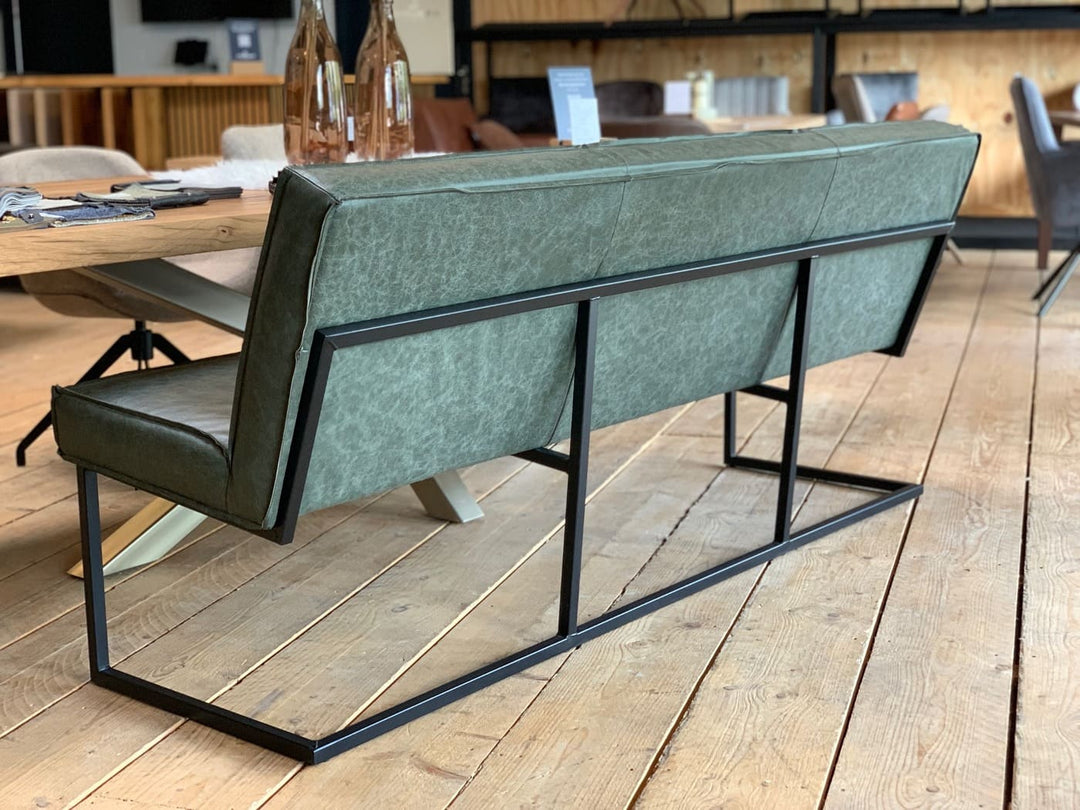 Schrägansicht einer modernen Sitzbank mit grünem Lederbezug und schwarzem Metallgestell vor einem Holztisch im Möbel-Showroom