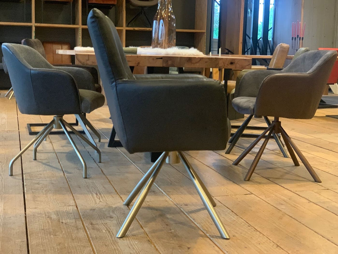 Lederstuhl drehbar mit hoher Rückenlehne aus schwarzem Leder und silbernem Untergestell in Seitenansicht, an einem Holztisch in moderner Esszimmerumgebung mit weiteren gepolsterten Stühlen auf hellem Holzboden.