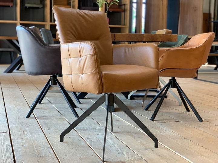 Moderner Lederstuhl hohe Rückenlehne drehbar in der Lederfarbe Cognac mit gepolsterter Sitzfläche, Armlehnen und dekorativer Steppung auf schwarzem Metall-Drehgestell, platziert an einem Holztisch in einem stilvollen Essbereich.