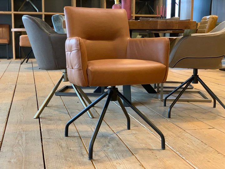 Moderner Lederstuhl-mit-Drehfunktion-119D in warmem Braunton mit gepolsterter Sitzfläche und Rückenlehne, auf einem schwarzen Metall-Drehgestell, platziert in einem stilvollen Innenraum mit Holzboden und weiteren Sitzmöbeln im Hintergrund.