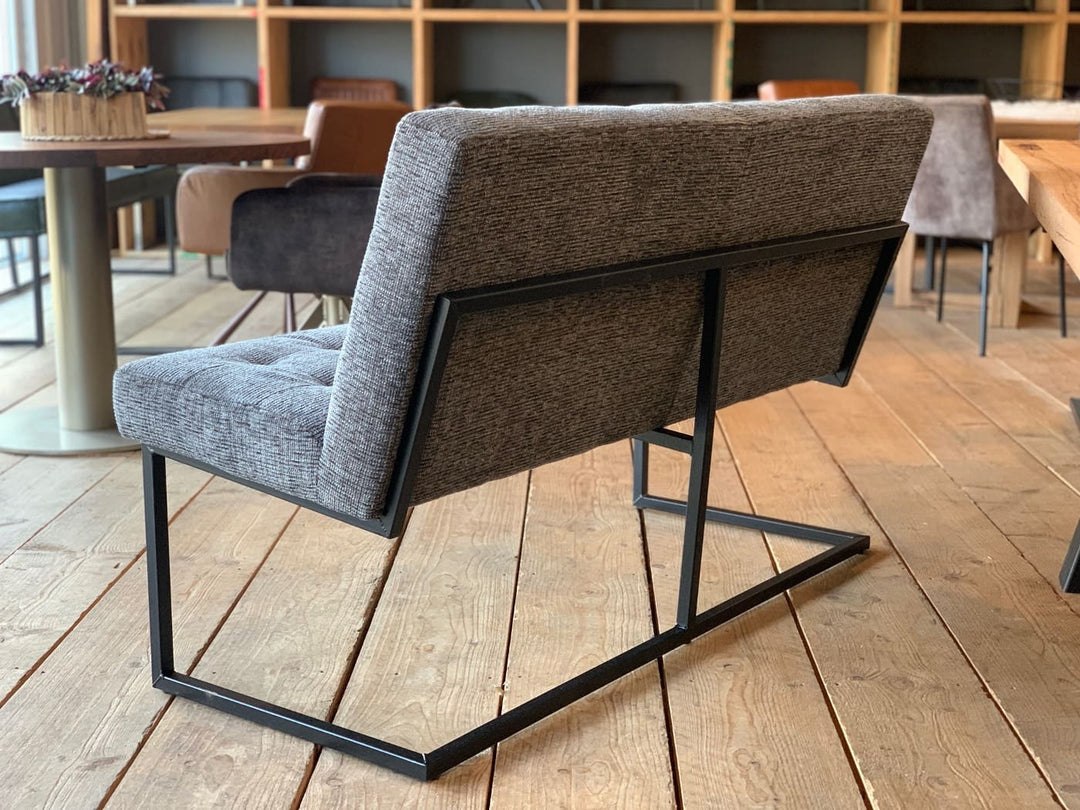 Moderne Sitzbank aus grauem Stoff mit gepolsterter Rückenlehne und schwarzem Metallgestell, Rückansicht im stilvollen Essbereich mit Holzboden