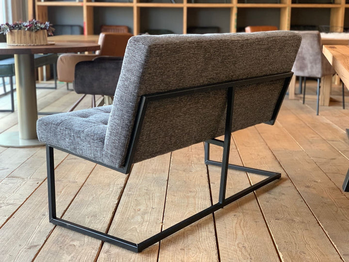Moderne Sitzbank aus grauem Stoff mit gepolsterter Rückenlehne und schwarzem Metallgestell, Rückansicht im stilvollen Essbereich mit Holzboden