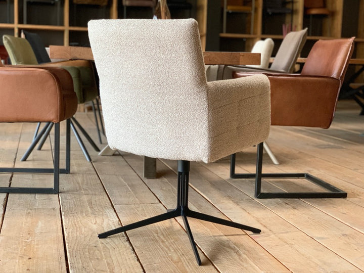 Rückansicht eines modernen, drehbaren Esszimmerstuhls mit Armlehnen. Die klare, leicht konisch zulaufende Rückenlehne unterstreicht das zeitgemäße Design, während der strukturierte Bouclé-Stoff dem Stuhl eine warme, wohnliche Ausstrahlung verleiht. Das schlanke, schwarze Metallgestell mit Drehfunktion sorgt für Stabilität und setzt einen stilvollen Kontrast zum hellen Bezug – ideal für ein harmonisches und modernes Esszimmerambiente.