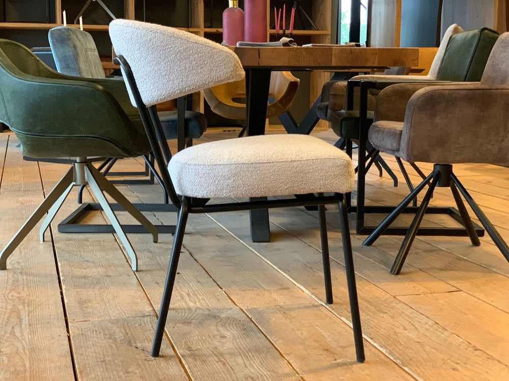 Moderner Küchen- und Gastrostuhl mit gepolsterter Sitz- und Rückenfläche in hellem Stoff sowie schwarzem Metallgestell, seitliche Ansicht im stilvollen Essbereich