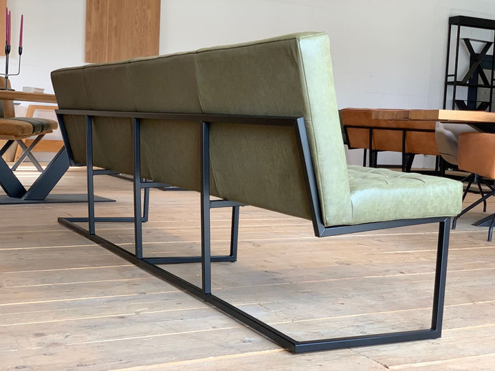 Rückansicht einer modernen Esszimmerbank aus olivgrünem Leder mit klaren Linien und schwarzem Metallgestell im Industrial-Stil, platziert auf hellem Holzboden im Essbereich
