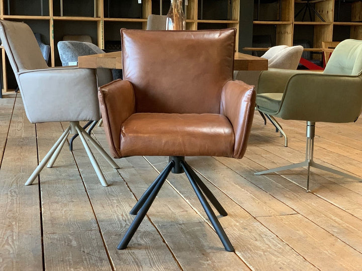 Vorderansicht eines drehbaren Polsterstuhls aus hochwertigem Leder in Braun, mit Armlehnen und modernem Metallgestell, stilvoll präsentiert in einem Showroom in Hamburg.