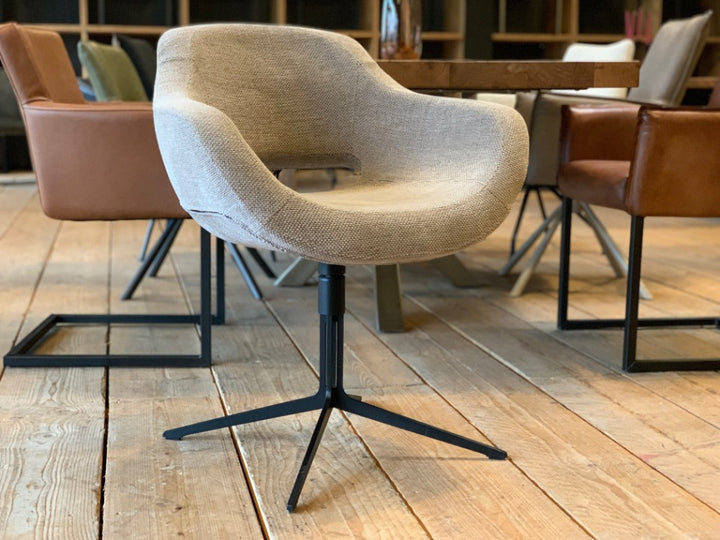Moderner Schalenstuhl mit ergonomisch geformter Sitzschale aus Stoff und elegantem Metall-Drehgestell, stilvoll kombiniert mit weiteren Esszimmerstühlen an einem Holztisch im Wohnambiente.