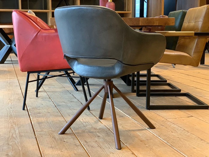 Rückansicht eines modernen Schalenstuhl drehbar Leder in grauer Ausführung mit weich gepolsterter Sitzschale und braunem Drehgestell, kombiniert mit weiteren farbigen Lederstühlen an einem Holztisch in einem stilvollen Essbereich.