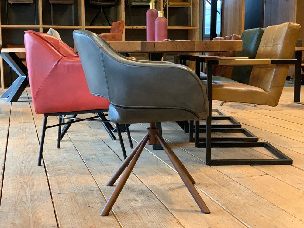 Seitliche Ansicht eines modernen Schalenstuhl drehbar Leder in grauer Ausführung mit ergonomisch geformter Sitzschale und braunem Drehgestell, platziert an einem Holztisch mit weiteren stilvollen Lederstühlen in einem wohnlichen Essbereich.