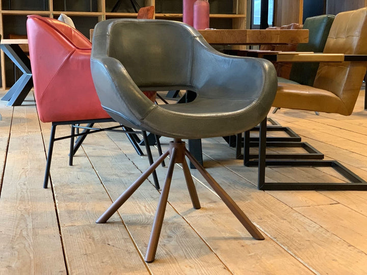 Moderner Schalenstuhl drehbar Leder in grauer Optik mit gepolsterter Sitzschale und braunem Metallgestell auf Holzfußboden, umgeben von weiteren stilvollen Esszimmerstühlen in warmen Farben in einem gemütlichen Innenraum.
