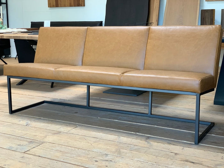Seitenansicht einer modernen Esszimmerbank mit braunem Lederbezug und schlankem schwarzem Metallgestell auf Holzboden im Möbel-Showroom
