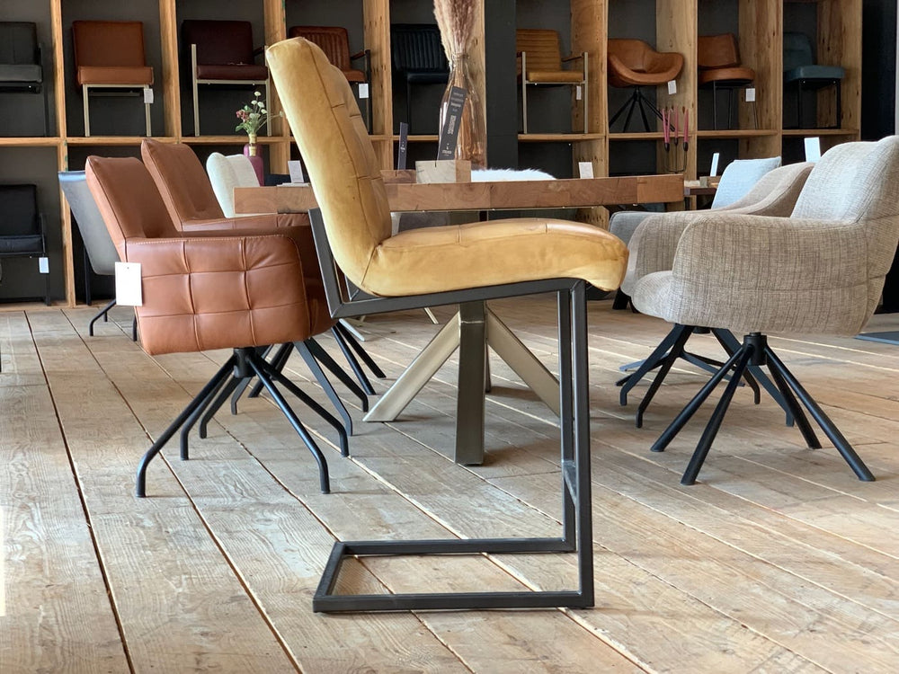 Thekenstuhl Leder Industrial in Mustard Seitenansicht: Moderner Thekenstuhl aus senfgelbem Leder mit gepolsterter Sitzfläche und Rückenlehne, getragen von einem schwarzen Metallgestell im Industrial-Stil, auf einem Holzboden in einem stilvollen Möbelgeschäft mit weiteren Sitzmöbeln im Hintergrund.