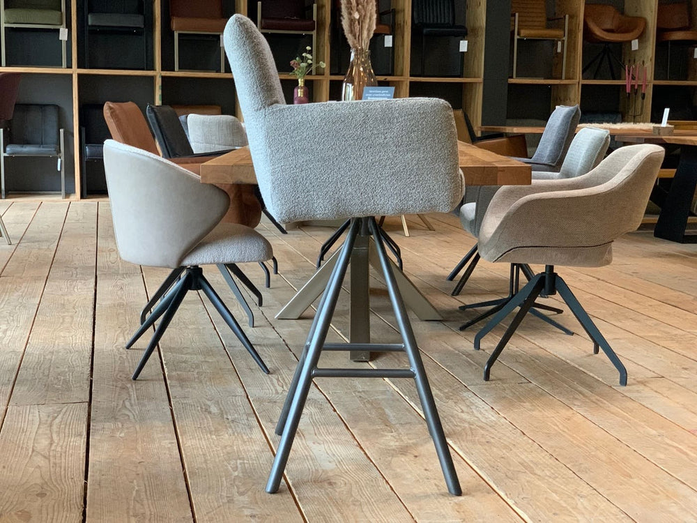 Drehbarer Thekenstuhl aus Stoff in Seitenansicht mit Armlehnen, gepolsterter Sitzschale und hoher Rückenlehne auf schwarzem Metall-Drehgestell in modernem Möbelshowroom.
