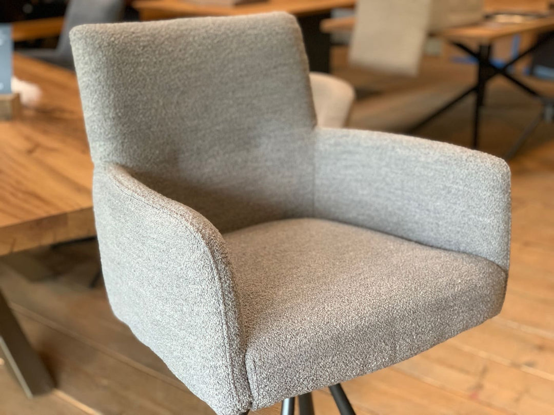 Drehbarer Thekenstuhl aus Stoff, Detailaufnahme der gepolsterten Sitzschale mit Armlehnen und hoher Rückenlehne in modernem Möbelshowroom.