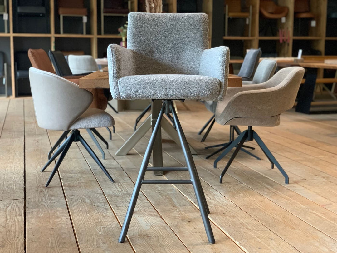 Drehbarer Thekenstuhl aus Stoff in Vorderansicht mit gepolsterter Sitzfläche, Armlehnen und hoher Rückenlehne auf schwarzem Metall-Drehgestell in modernem Möbelshowroom.